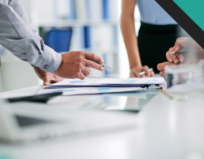 A close-up view of hands engaged in a business discussion over documents on a table, including charts and graphs, in a professional setting.