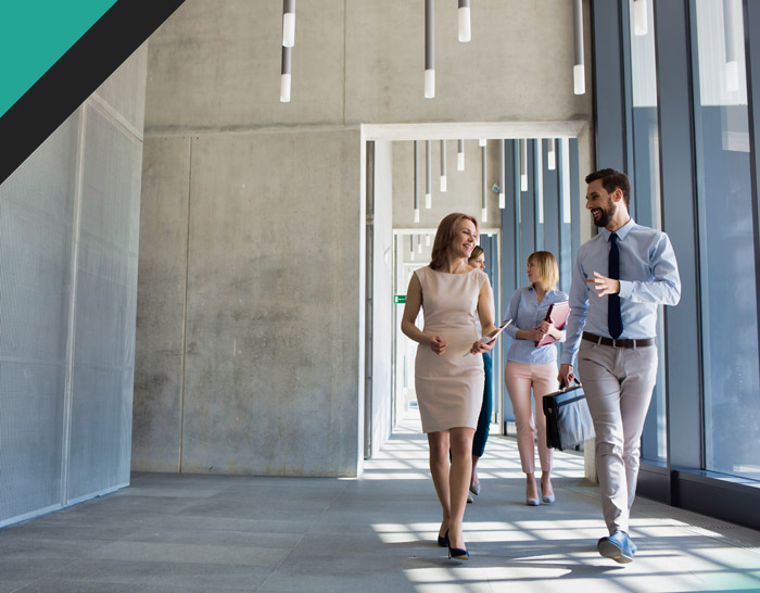 Group of professionals walking and discussing in a modern office hallway, featuring bright lighting and contemporary design.