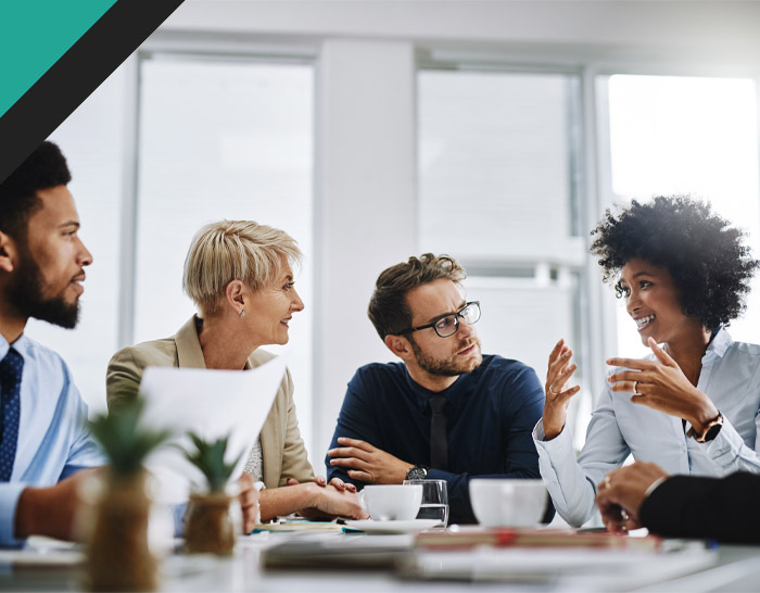 Group of diverse professionals engaged in a discussion around a conference table, with coffee cups and documents present, highlighting teamwork and collaboration.