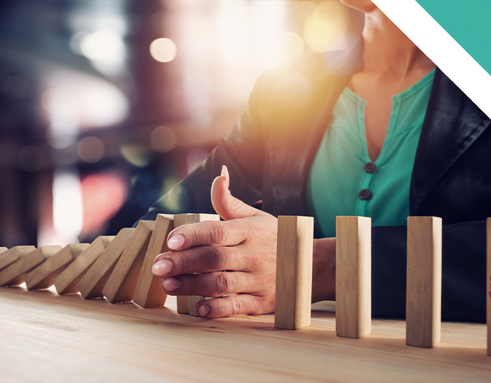 A person in a jacket and turquoise top is placing their hands near a row of wooden dominoes, suggesting a moment of focus and strategy in a bright, softly lit environment.