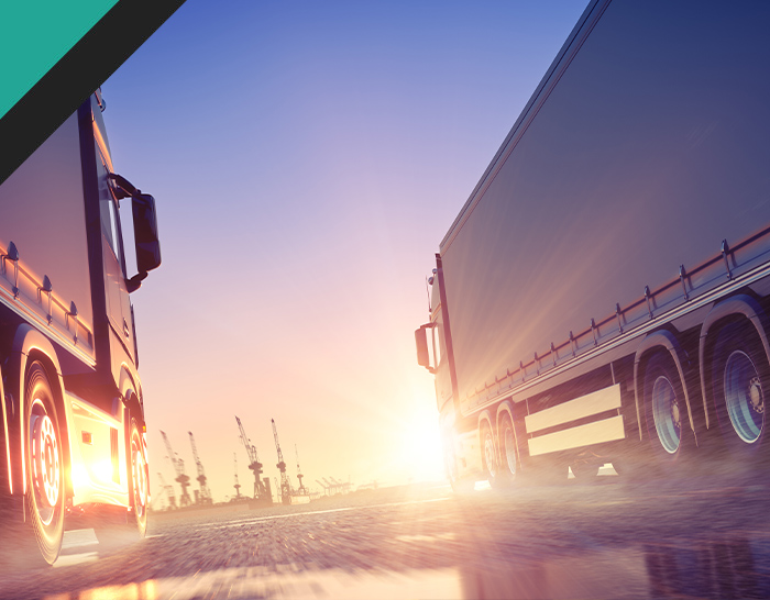 two trucks driving towards a sunset with a hazy background, symbolizing logistics and transportation industry