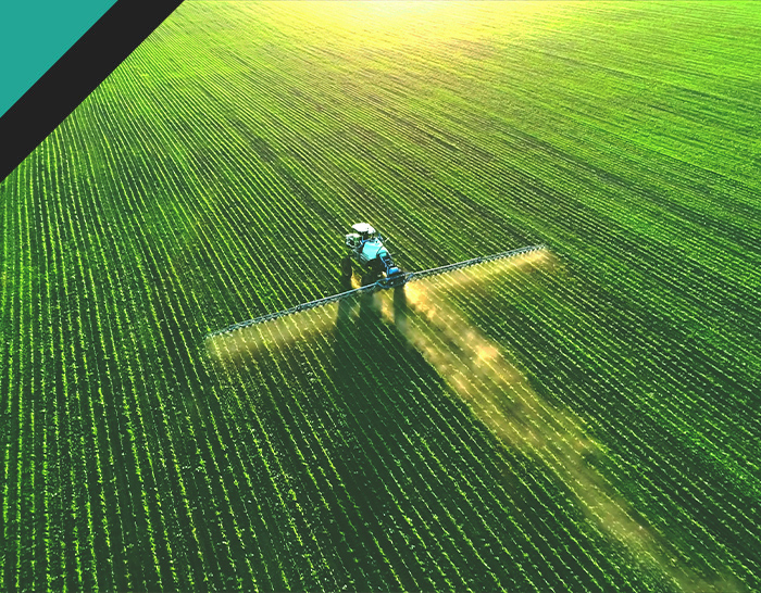 Aerial view of a tractor spraying fertilizers across a lush green field, illustrating agricultural practices and crop health management.