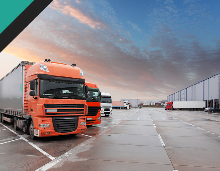 Trucks parked in a logistics yard at sunset, showcasing several large vehicles, including an orange truck, against a cloudy sky. Ideal for transportation industry visuals.