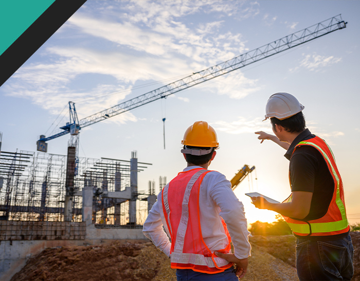 Construction workers discussing plans at sunset near a building site with a crane in the background and a focus on safety.