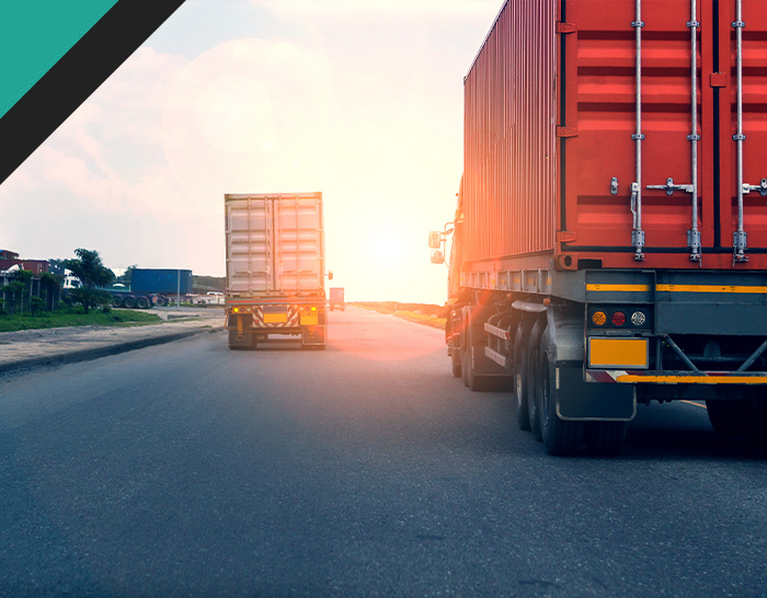 Two trucks driving on a road towards a sunset, with shipping containers visible on their trailers, highlighting the logistics and transportation industry.