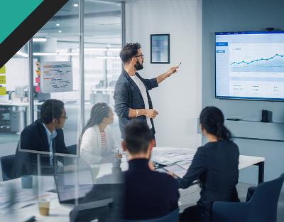 Business meeting with a presenter pointing at a growth chart on a screen, surrounded by attentive colleagues engaged in discussion and analysis.