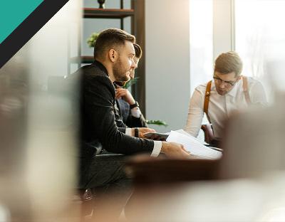 Three professionals engaged in a meeting, analyzing documents in a modern office setting. The focus is on collaboration and strategic planning.